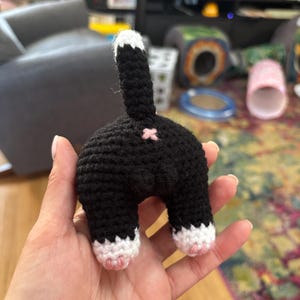 May include: A black and white crocheted cat toy with pink paw pads. The cat is sitting up with its tail in the air.