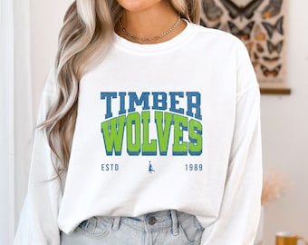 May include: White long-sleeve sweatshirt with a green and blue graphic that says "TIMBER WOLVES ESTD 1989".