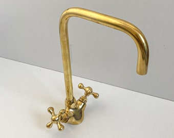 May include: A gold-colored kitchen faucet with a curved spout and cross-shaped handles. The faucet is made of brass and has a vintage or antique style. The design is suitable for a kitchen or bar sink.