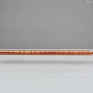 May include: A horizontal copper towel bar featuring a cylindrical rod with a repeating etched chevron pattern. The bar is supported by two curved mounting brackets on each end, each with a circular base plate containing a screw hole.