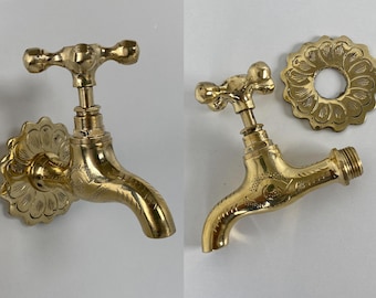 May include: Two ornate brass outdoor faucets with decorative floral details. The faucet on the left has a wall mount with a floral design. The faucet on the right has a separate floral design wall mount.