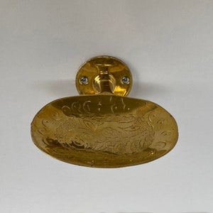 May include: A gold-colored soap dish with an ornate design. The dish is mounted to a wall with two screws.
