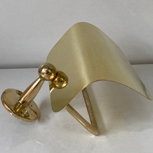 May include: A gold-toned metal toilet paper holder with a curved, flat top and a round base. The holder is mounted to a wall.