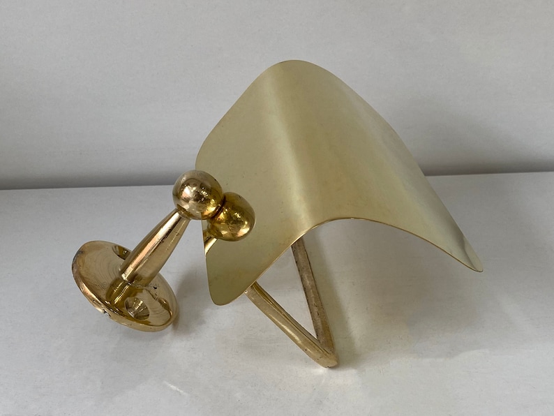 May include: A gold-toned metal toilet paper holder with a curved, flat top and a round base. The holder is mounted to a wall.