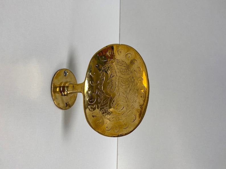 May include: A gold-toned metal wall hook with an ornate design. The hook is attached to a round base and has a curved arm.