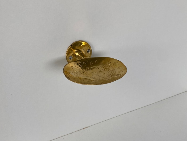 May include: A gold-toned door handle with an ornate, engraved design. The handle is shaped like a shallow bowl.