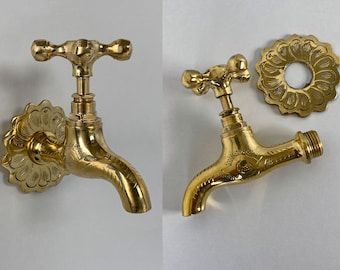 May include: Two ornate brass faucets with a cross-shaped handle and a decorative floral design. The faucet on the left is mounted to a wall with a matching floral design. The faucet on the right is shown with a separate floral design that can be used as a wall mount.