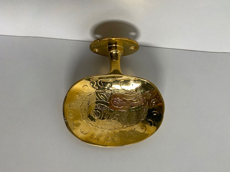 May include: A gold-toned metal door handle with an oval-shaped plate featuring an intricate floral design.
