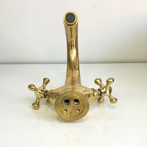 Op de afbeelding: Een gouden kraan met twee handvatten en een versierd ontwerp. De kraan heeft een gebogen uitloop en is ontworpen voor een wastafel.