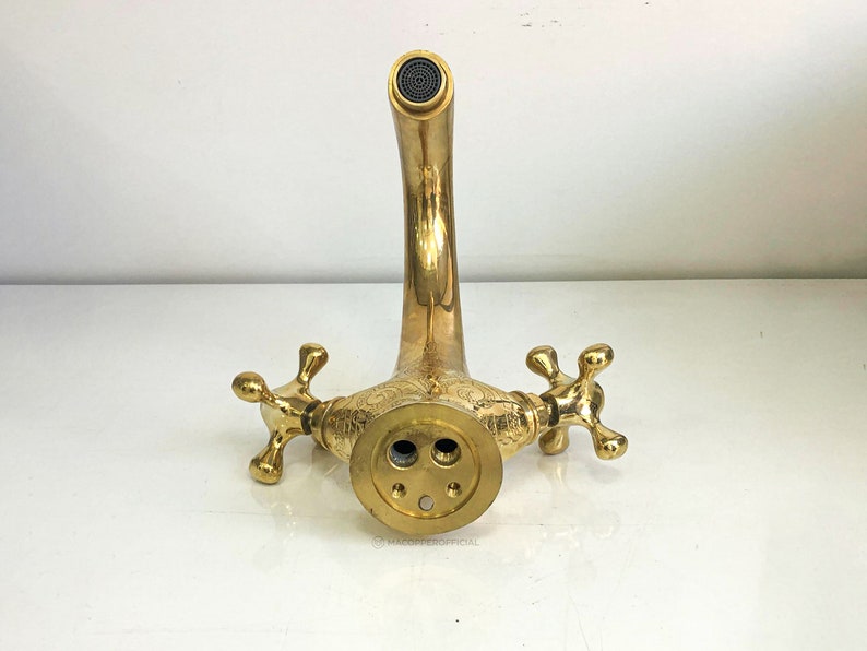 Op de afbeelding: Een gouden kraan met twee handvatten en een versierd ontwerp. De kraan heeft een gebogen uitloop en is ontworpen voor een wastafel.
