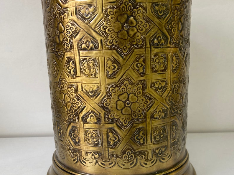 May include: A gold metal vase with an intricate embossed pattern of flowers and geometric shapes.