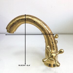 Op de afbeelding: Gouden kraan met een sierlijk ontwerp. De kraan is 14 cm breed en 16,5 cm hoog.