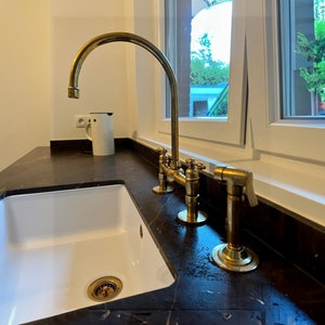 May include: A white porcelain kitchen sink with a gold faucet and a black granite countertop.