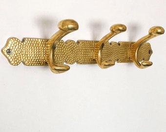 May include: Gold metal coat rack with three hooks. The rack has a textured surface and a decorative design.