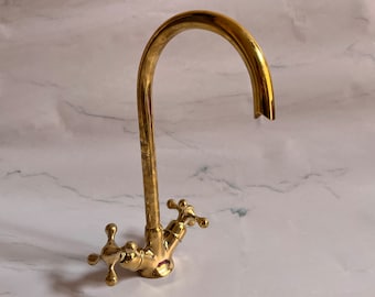 May include: A gold-toned kitchen faucet with a high arc spout and two cross-shaped handles.
