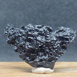 May include: A black, rough, and textured meteorite with a unique, irregular shape. The meteorite is displayed on a white stand.