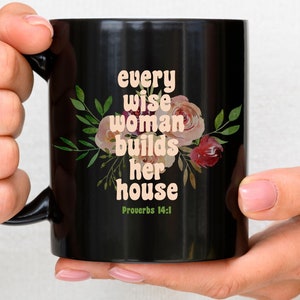 May include: Black coffee mug with a white floral design and the text "every wise woman builds her house Proverbs 14:1"