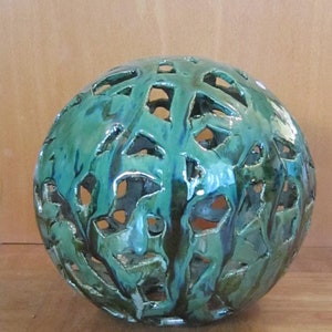 Może przedstawiać: Zielono-niebieska ceramiczna kula z ozdobnym wzorem wyciętym. Kula ma błyszczące wykończenie i jest wykonana z fakturowanego materiału.