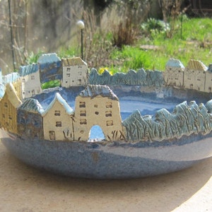 Peut inclure: Un bol en céramique bleu avec une scène d'une petite ville avec des maisons et des arbres. Le bol est émaillé dans un schéma de couleurs bleu et blanc.