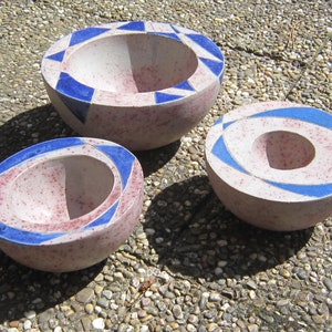 Può includere: Tre ciotole in ceramica con una glassa rosa macchiata e disegni geometrici blu. Le ciotole sono annidate l'una dentro l'altra, con la ciotola più grande in cima e la ciotola più piccola in fondo.