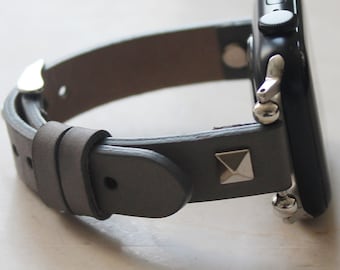 May include: A smartwatch with a black rectangular case and a grey leather strap. The strap features a single silver-toned pyramid stud near the attachment point and a silver-toned metal buckle. The watch is shown from a side profile angle.