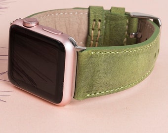 May include: A smartwatch with a rose gold metallic casing and a black screen, featuring a textured olive green leather strap with visible light green stitching and a silver-toned metal buckle closure.
