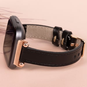 May include: A black leather watch strap with rose gold accents and a square-shaped watch face.