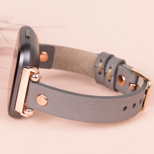 May include: A grey leather watch strap with rose gold fittings and a black watch face.
