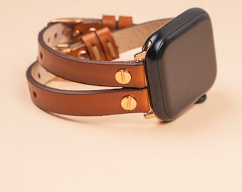 May include: A black smartwatch with a rectangular screen and a double-wrap brown leather strap. The strap features gold-toned metal hardware, including two circular studs near the watch face and a buckle closure with multiple adjustment holes.