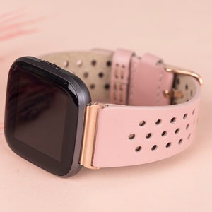 Puede incluir: Una correa de reloj de cuero rosa con una esfera negra y detalles en oro rosa. La correa tiene un dise&ntilde;o perforado.