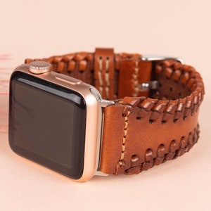 May include: A brown leather Apple Watch band with a braided design and white stitching. The band is shown on a rose gold Apple Watch.
