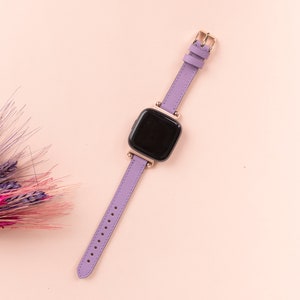 May include: A purple leather watch band with a gold buckle and a black square watch face.