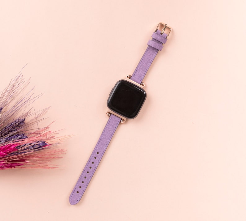 May include: A purple leather watch band with a gold buckle and a black square watch face.
