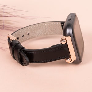 May include: A black leather watch strap with rose gold accents and a black square watch face.