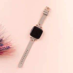 May include: A gray leather watch band with a rose gold buckle and a square black watch face.