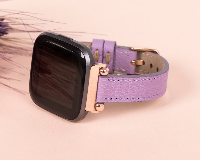 May include: A purple leather watch band with rose gold accents and a black smartwatch.