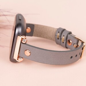 May include: A gray leather watch band with rose gold hardware and a black watch face.
