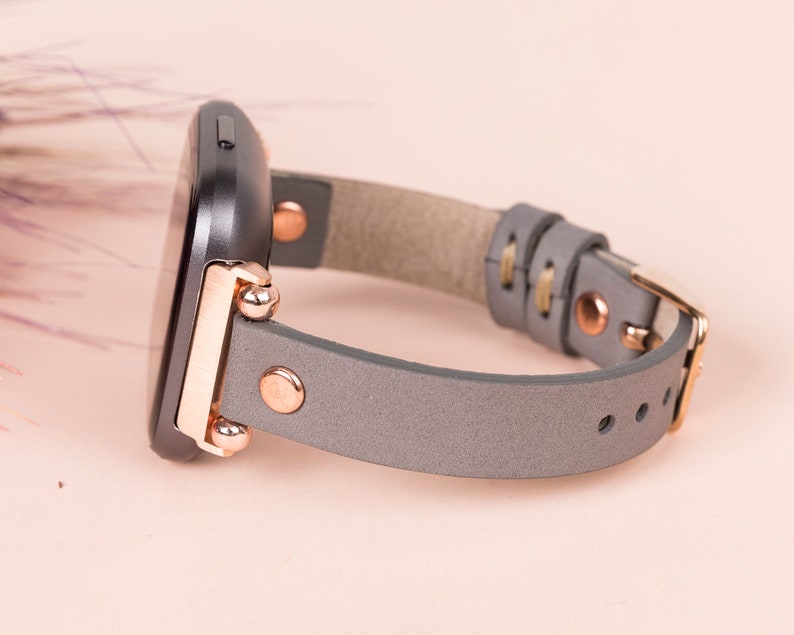 May include: A gray leather watch band with rose gold hardware and a black watch face.