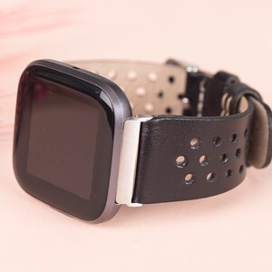 May include: A black leather watch strap with a perforated design and a silver buckle. The watch face is black and rectangular.