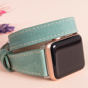 May include: A light green leather watch strap with white stitching wraps around a rose gold Apple Watch.