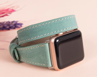 May include: A smartwatch with a rose gold casing and a black screen, featuring a double-wrap sage green leather band with visible light-coloured stitching along the edges. The band wraps around the watch body, creating a layered appearance.