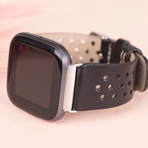 May include: A black leather watch strap with a perforated design and a silver buckle. The watch face is black and rectangular.