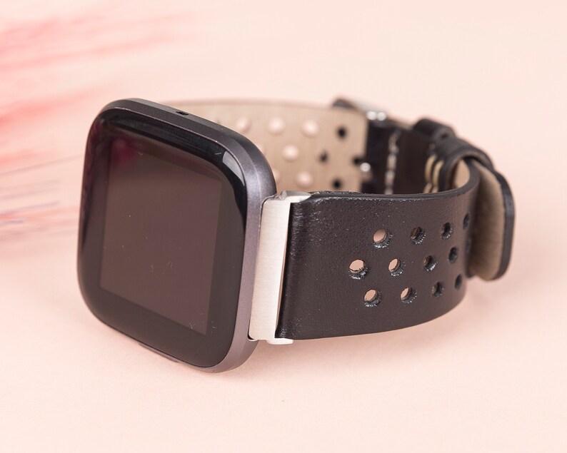 May include: A black leather watch strap with a perforated design and a silver buckle. The watch face is black and rectangular.