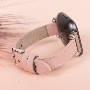 K&ouml;nnte beinhalten: Ein rosafarbenes Lederarmband mit silbernen Beschl&auml;gen und einem schwarzen Zifferblatt.