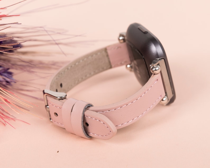 K&ouml;nnte beinhalten: Ein rosafarbenes Lederarmband mit silbernen Beschl&auml;gen und einem schwarzen Zifferblatt.