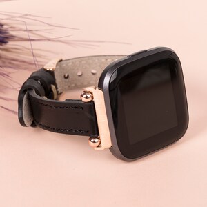 May include: A black leather watch strap with rose gold accents and a black smartwatch face.