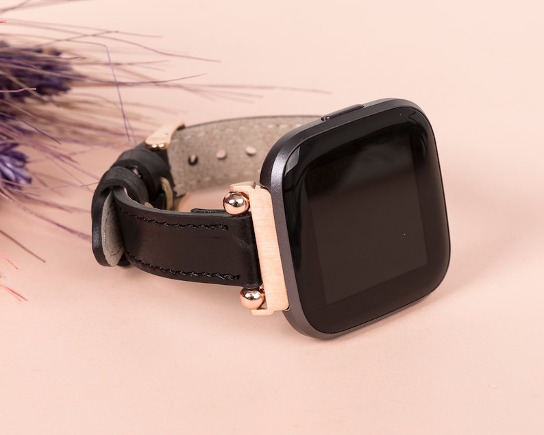 May include: A black leather watch strap with rose gold accents and a black smartwatch face.