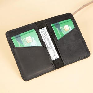 Peut inclure: Un portefeuille en cuir noir avec deux emplacements pour cartes et une poche pour l'argent liquide. Le portefeuille contient deux cartes de cr&eacute;dit vertes avec le texte "Cardno" et "1234" visible.