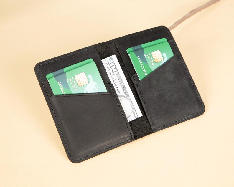 Peut inclure: Un portefeuille en cuir noir avec deux emplacements pour cartes et une poche pour l'argent liquide. Le portefeuille contient deux cartes de cr&eacute;dit vertes avec le texte "Cardno" et "1234" visible.
