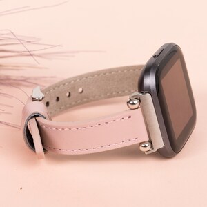 May include: A pink leather watch band with silver accents and a black smartwatch face.